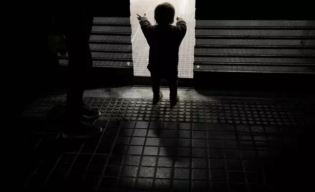 Felipe reaches through the door of a bakery where his parents Walter and Evelyn wait to take home discarded baked goods that the shop didn't sell in Buenos Aires, Argentina, Tuesday, Sept. 3, 2024. (AP Photo/Natacha Pisarenko)