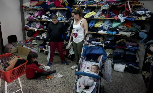 Rocio Costa watches her daughter Francesca try on shoes at a second-hand clothing fair alongside her other children Almendra and Tiziano in Buenos Aires, Argentina, Monday, Sept. 16, 2024. (AP Photo/Natacha Pisarenko)