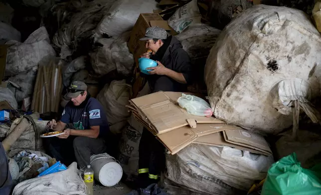 Trash pickers Jose Oman Toledo and Hernan Cardozo eat lunch after cooking for a large group of fellow workers at the recycling plant where they retrieve sellable items in Lujan, Argentina, Thursday, Aug. 29, 2024. (AP Photo/Natacha Pisarenko)