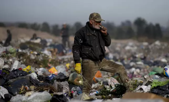 An elderly man pauses to smoke a cigarette as he sifts through garbage at a landfill in search of materials to sell in Lujan, Argentina, Thursday, Aug. 29, 2024. (AP Photo/Natacha Pisarenko)