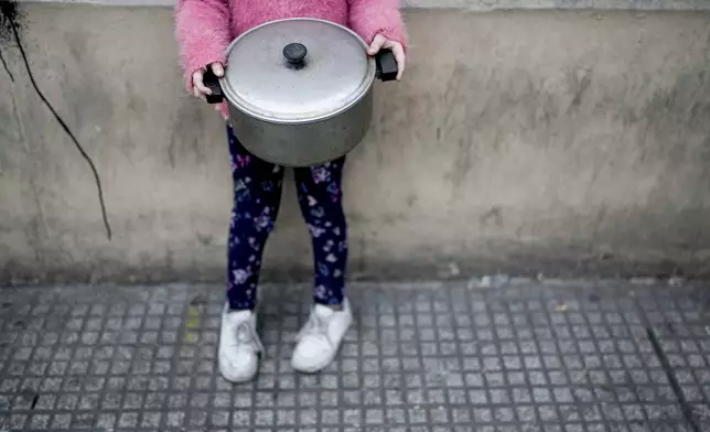 A little girl clutches her pot outside a soup kitchen where she waits in line for her turn to collect a free, cooked meal to take home in Buenos Aires, Argentina, Monday, Sept. 9, 2024. (AP Photo/Natacha Pisarenko)