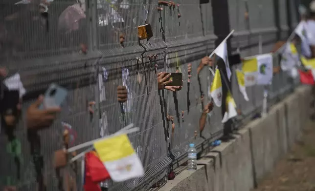 People try to film Pope Francis with their mobile phones through a fence in Dili, East Timor, Monday, Sept. 9, 2024. (AP Photo/Dita Alangkara)