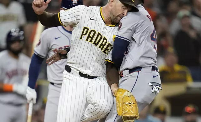 Houston Astros' Yordan Alvarez, right, runs into San Diego Padres relief pitcher Jason Adam, center, as he scores off a wild pitch during the eighth inning of a baseball game Tuesday, Sept. 17, 2024, in San Diego. (AP Photo/Gregory Bull)