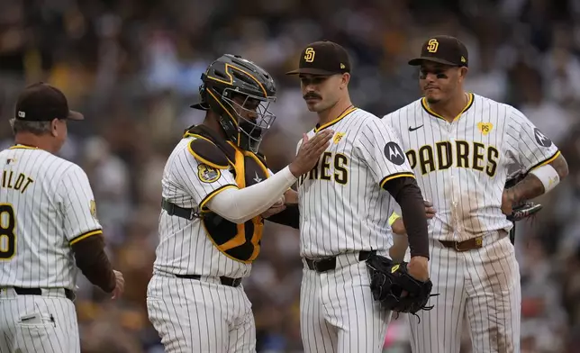 San Diego Padres catcher Elias Diaz, second from left, pats starting pitcher Dylan Cease on the chest as Cease exits and third baseman Manny Machado looks on, right, during the ninth inning of a baseball game against the Houston Astros Wednesday, Sept. 18, 2024, in San Diego. (AP Photo/Gregory Bull)