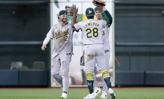 From left, Oakland Athletics' Max Schuemann (12), Daz Cameron (28) and J.J. Bleday celebrate their win in 12 innings against the Houston Astros after a baseball game Tuesday, Sept. 10, 2024, in Houston. (AP Photo/Michael Wyke)