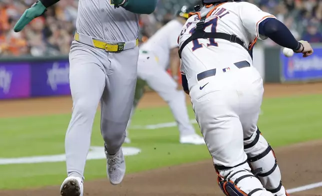 Oakland Athletics' Brent Rooker, left, scores on the sacrifice fly by Shea Langeliers as Houston Astros catcher Victor Caratini reaches for the ball during the first inning of a baseball game, Tuesday, Sept. 10, 2024, in Houston. (AP Photo/Michael Wyke)