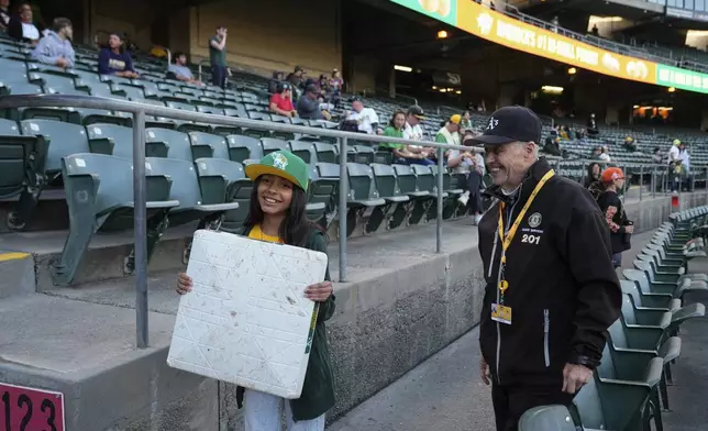 Leland Anderson, right, watches as 10-year-old Jordyn Alvarado poses for a photograph with a base from a baseball game between the Colorado Rockies and the Oakland Athletics, Wednesday, May 22, 2024, in Oakland, Calif. (AP Photo/Godofredo A. Vásquez)