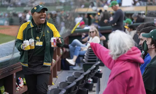 Derrick Smith, left, smiles as he delivers drinks for fans sitting in his section during a baseball game between the Colorado Rockies and the Oakland Athletics, Wednesday, May 22, 2024, in Oakland, Calif. (AP Photo/Godofredo A. Vásquez)