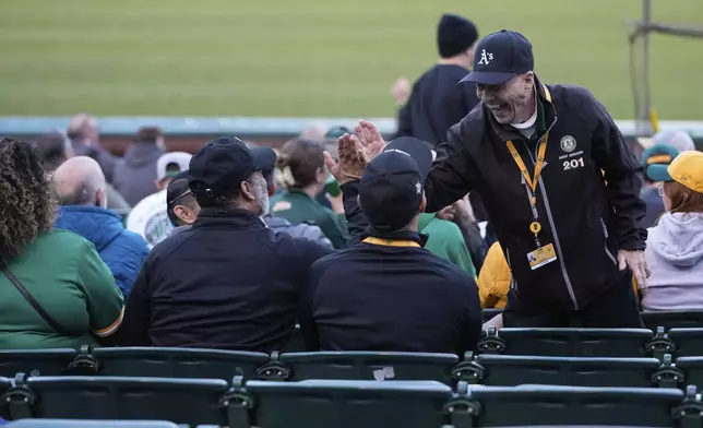 Leland Anderson, right, high-fives a fan during a baseball game between the Colorado Rockies and the Oakland Athletics, Wednesday, May 22, 2024, in Oakland, Calif. (AP Photo/Godofredo A. Vásquez)