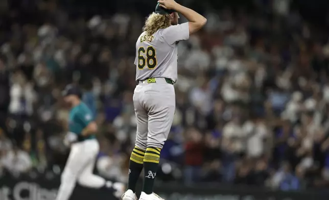 Oakland Athletics starting pitcher Joey Estes (68) adjusts his cap on the mound after giving up a solo home run to Seattle Mariners' Cal Raleigh, back left, who runs the bases during the fourth inning in a baseball game, Saturday, Sept. 28, 2024, in Seattle. (AP Photo/John Froschauer)