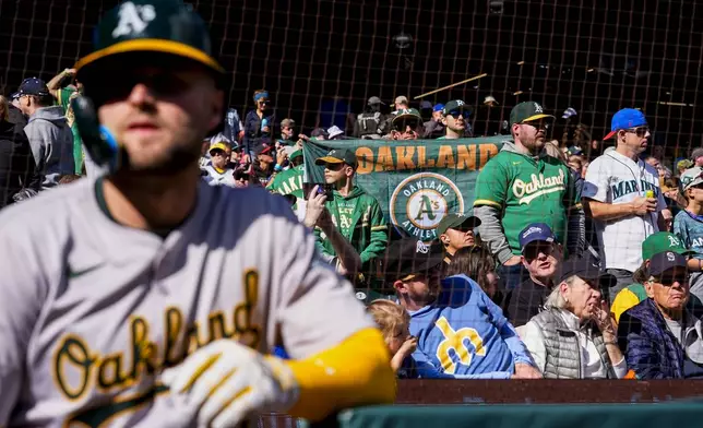 A fan waves an Oakland Athletics flag as Oakland Athletics' Seth Brown stands at the railing before a baseball game, Sunday, Sept. 29, 2024, in Seattle. (AP Photo/Lindsey Wasson)