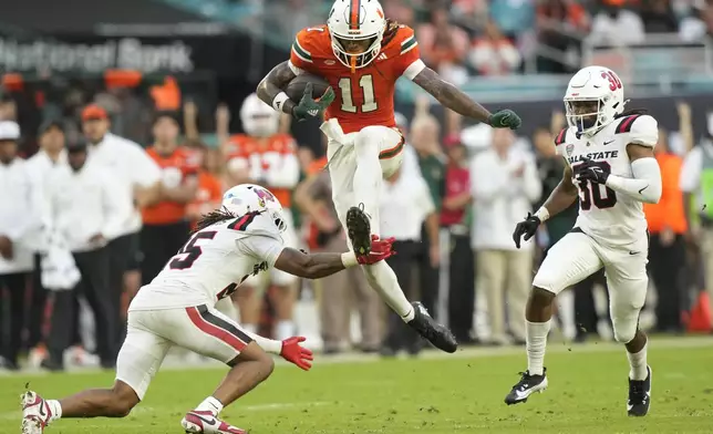 Miami wide receiver Samuel Brown (11) runs for a first down as Ball State defensive back Elijah Davis, left, and defensive back Jalon Jones (30) defend during the first half of an NCAA football game, Saturday, Sept. 14, 2024, in Miami Gardens, Fla. (AP Photo/Lynne Sladky)