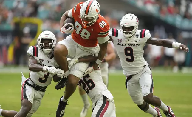 Miami tight end Riley Williams (88) runs for a first down as Ball State defensive back DD Snyder (3), cornerback Myles Norwood (26), and linebacker Keionte Newson (9) defend during the first half of an NCAA football game, Saturday, Sept. 14, 2024, in Miami Gardens, Fla. (AP Photo/Lynne Sladky)