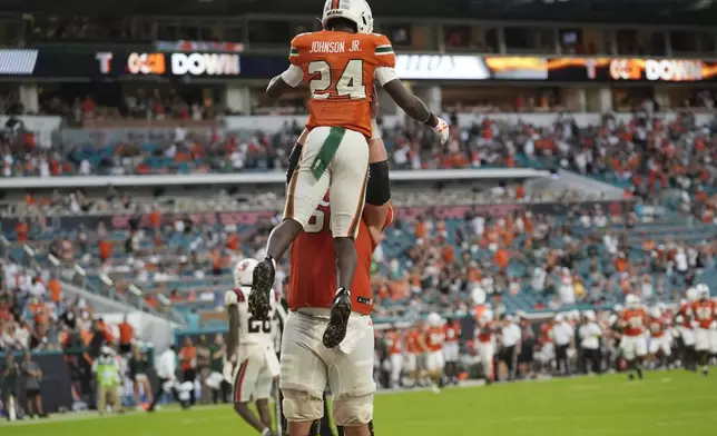 Miami running back Chris Johnson Jr. (24) is lifted into the air by center Zach Carpenter after scoring a touchdown during the first half of an NCAA football game against Ball State, Saturday, Sept. 14, 2024, in Miami Gardens, Fla. (AP Photo/Lynne Sladky)