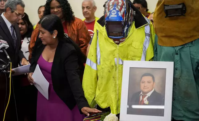 Maria del Carmen Castellón, the wife of Miguel Luna, a welder who died during the collapse of Baltimore's Francis Scott Key Bridge, places a rose near a portrait of her husband and his welding gear before speaking during a press conference, Tuesday, Sept. 17, 2024, in Baltimore. (AP Photo/Stephanie Scarbrough)