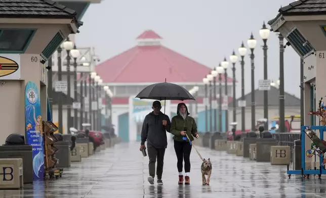 FILE - A couple walk in the rain with their dog along the Huntington Beach Pier in Huntington Beach, Calif., on Feb. 6, 2024. (AP Photo/Marcio Jose Sanchez, File)