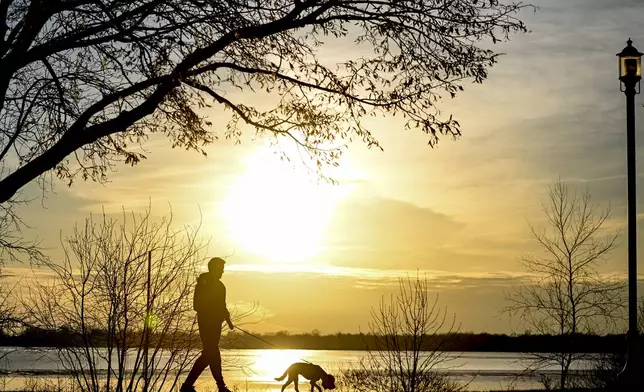 FILE - The sun sets behind a person as they walk their dog along Lac Saint-Louis in Montreal, on. March 3, 2024. (Graham Hughes/The Canadian Press via AP)