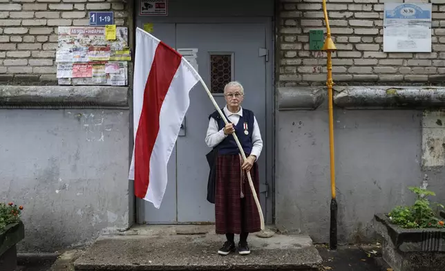 FILE - Nina Bahinskaya, 73, poses for a photo holding a flag that became the symbole of the opposition at an entrance of her apartment building in Minsk, Belarus, on Sept. 10, 2020. (AP Photo, File)