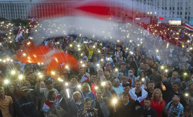 FILE - Protesters shine the lights on their phones and wave red-and-white flags that became symbols of the opposition during an anti-government demonstration in Independence Square in Minsk, Belarus, on Aug. 19, 2020. (AP Photo, File)