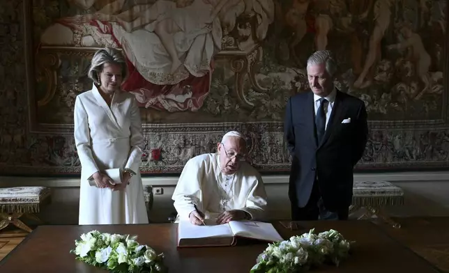 Pope Francis, center, signs the book of honor during his visit to King Philippe of Belgium, right, and Queen Mathilde at the Castle of Laeken, Belgium, Friday, Sept. 26, 2024, on the second day of a four-day apostolic journey to Luxembourg and Belgium. (Alberto Pizzoli/pool photo via AP)