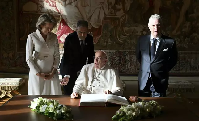 Pope Francis, center, signs the book of honor during his visit to King Philippe of Belgium, right, and Queen Mathilde at the Castle of Laeken, Belgium, Friday, Sept. 26, 2024, on the second day of a four-day apostolic journey to Luxembourg and Belgium. (Alberto Pizzoli/pool photo via AP)