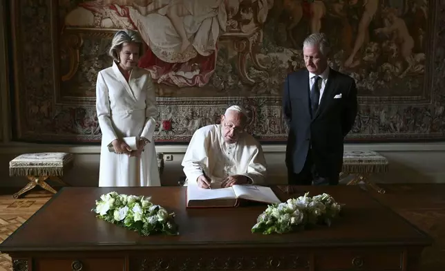 Pope Francis, center, signs the book of honor during his visit to King Philippe of Belgium, right, and Queen Mathilde at the Castle of Laeken, Belgium, Friday, Sept. 26, 2024, on the second day of a four-day apostolic journey to Luxembourg and Belgium. (Alberto Pizzoli/pool photo via AP)