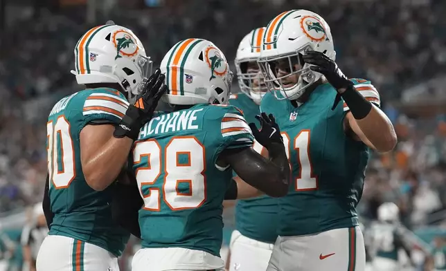 Miami Dolphins running back De'Von Achane (28) is congratulated by his teammates after scoring a touchdown during the first half of an NFL football game against the Buffalo Bills, Thursday, Sept. 12, 2024, in Miami Gardens, Fla. (AP Photo/Lynne Sladky)