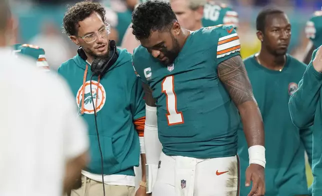 Miami Dolphins head coach Mike McDaniel talks to quarterback Tua Tagovailoa (1) as he leaves the game after suffering a concussion during the second half of an NFL football game against the Buffalo Bills, Thursday, Sept. 12, 2024, in Miami Gardens, Fla. (AP Photo/Rebecca Blackwell)