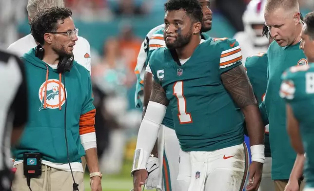 Miami Dolphins head coach Mike McDaniel talks to quarterback Tua Tagovailoa (1) as he leaves the game after suffering a concussion during the second half of an NFL football game against the Buffalo Bills, Thursday, Sept. 12, 2024, in Miami Gardens, Fla. (AP Photo/Rebecca Blackwell)