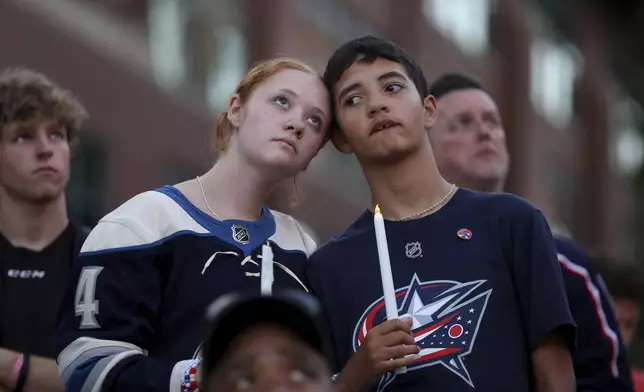 Blue Jackets fans Gianna,left, and Elijah Willis, have a moment of silence during the candlelight vigil to honor Columbus Blue Jackets hockey player Johnny Gaudreau, outside of Nationwide Arena in Columbus, Ohio, Thursday, Sept. 4, 2024. Gaudreau and his brother Matthew were killed by a motor vehicle last week while riding bicycles. (AP Photo/Joe Maiorana)