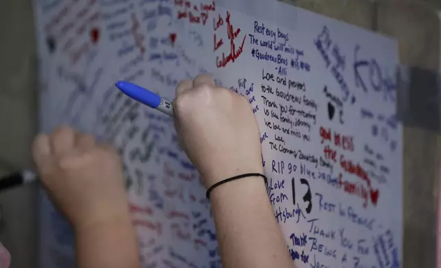 Fans write messages during a candlelight vigil to honor Columbus Blue Jackets hockey player Johnny Gaudreau, Thursday, Sept. 4, 2024, outside of Nationwide Arena in Columbus, Ohio. Gaudreau and his brother Matthew were killed by a motor vehicle last week while riding bicycles. (AP Photo/Joe Maiorana)