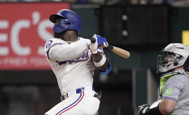 Texas Rangers' Adolis Garcia follows through on a two-run single as Toronto Blue Jays catcher Alejandro Kirk, right, looks on in the fourth inning of a baseball game in Arlington, Texas, Tuesday, Sept. 17, 2024. (AP Photo/Tony Gutierrez)