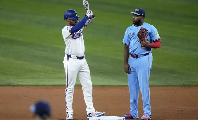 Texas Rangers' Marcus Semien, left, celebrates his double as Toronto Blue Jays' Vladimir Guerrero Jr., right, looks on in the first inning of a baseball game in Arlington, Texas, Wednesday, Sept. 18, 2024. (AP Photo/Tony Gutierrez)