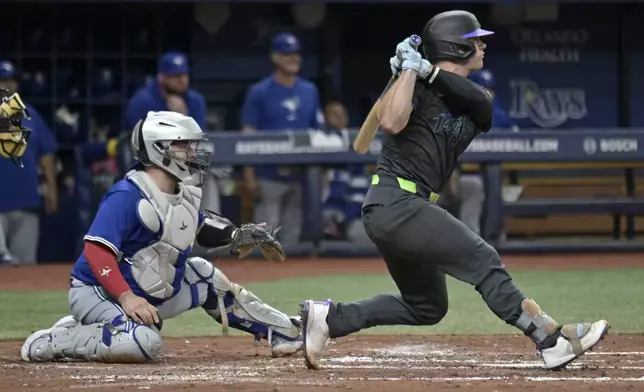 Toronto Blue Jays catcher Alejandro Kirk, left, looks on as Tampa Bay Rays' Ben Rortvedt, right, hits an RBI-single during the second inning of a baseball game Saturday, Sept. 21, 2024, in St. Petersburg, Fla. (AP Photo/Steve Nesius)