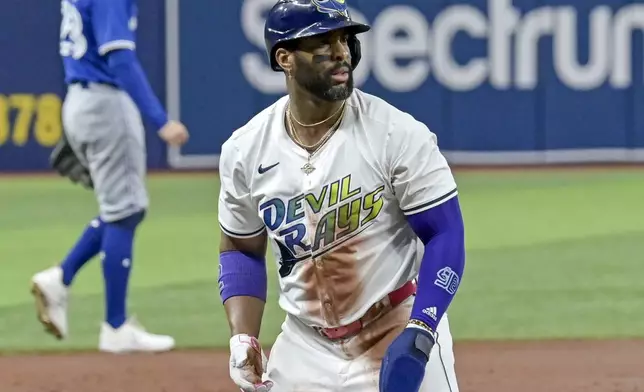 Tampa Bay Rays' Yandy Diaz, foreground, kneels on the bag after reaching third base on a passed ball by Toronto Blue Jays catcher Alejandro Kirk during the first inning of a baseball game Friday, Sept. 20, 2024, in St. Petersburg, Fla. (AP Photo/Steve Nesius)