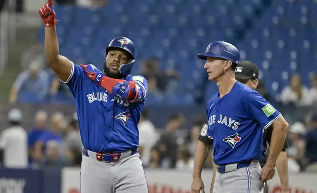 Toronto Blue Jays first base coach Mark Budzinski, front right, looks on as Vladimir Guerrero Jr., left, gestures toward the dugout after hitting a single to center field off Tampa Bay Rays starter Tyler Alexander during the first inning of a baseball game Friday, Sept. 20, 2024, in St. Petersburg, Fla. (AP Photo/Steve Nesius)