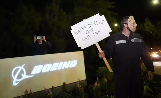 A Boeing worker wears a mask while holding a "happy strike day" sign after union members voted overwhelmingly to reject a contract offer and go on strike Friday, Sept. 13, 2024, outside the company's factory in Renton, Wash. (AP Photo/Lindsey Wasson)