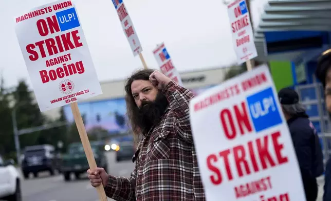 Jacob Bustad, a machinist who has worked for Boeing for 14 years, holds up a fist to passing drivers as union members work the picket line after voting to reject a contract offer and go on strike, Sunday, Sept. 15, 2024, near the company's factory in Everett, Wash. (AP Photo/Lindsey Wasson)