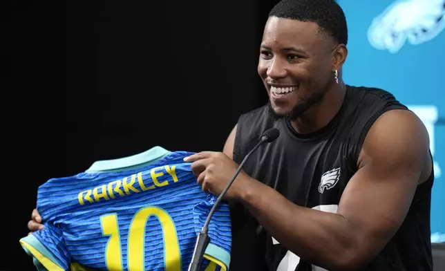 Philadelphia Eagles Saquon Barkley holds up a Brazilian national soccer jersey with his name on it, during a press conference ahead of a game against the Green Bay Packers at the Neo Quimica Arena in Sao Paulo, Thursday, Sept. 5, 2024. (AP Photo/Andre Penner)