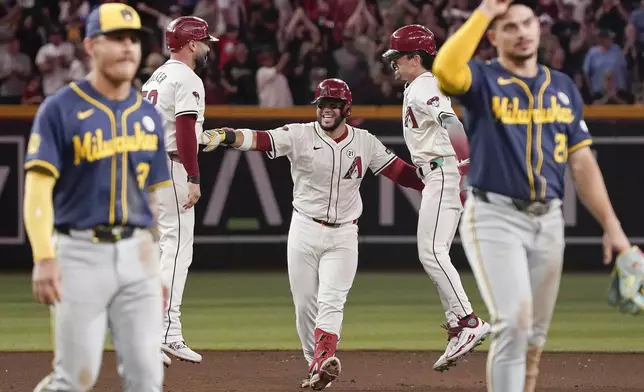 Milwaukee Brewers third baseman Joey Ortiz, front left, and shortstop Willy Adames, front right, walk off the field as Arizona Diamondbacks' Christian Walker, second from left, and Corbin Carroll, second from right, celebrate after a walkoff single by Eugenio Suárez, center, in the bottom of the 10th inning of a baseball game Sunday, Sept. 15, 2024, in Phoenix. (AP Photo/Darryl Webb)