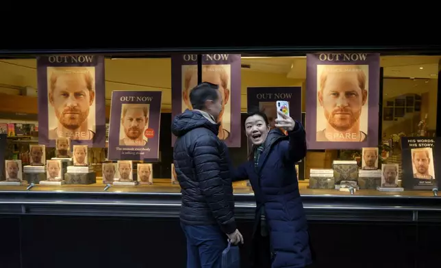 FILE - A couple take a photograph in front of a display of copies of Prince Harry's book 'Spare" in the window of a book shop in London, Tuesday, Jan. 10, 2023. (AP Photo/Kirsty Wigglesworth, File)