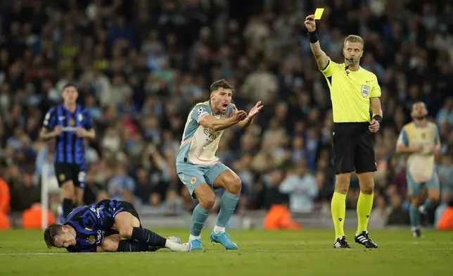 Manchester City's Ruben Dias, center, reacts as referee Glenn Nyberg, right, shows him a yellow card after he fouled Inter Milan's Piotr Zielinski, left, during the Champions League opening phase soccer match between Manchester City and Inter Milan at the Etihad Stadium, in Manchester, England, Wednesday, Sept. 18, 2024. (AP Photo/Dave Thompson)