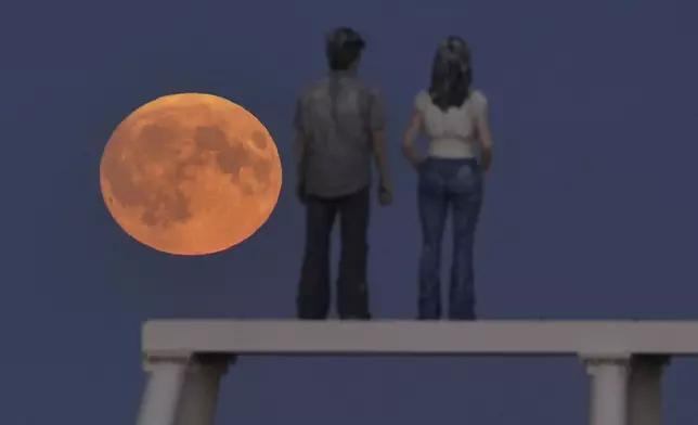 The full Harvest moon rises over 'The Couple' sculpture at Newbiggin-by-the-Sea in Northumberland, Tuesday Sept. 17, 2024. (Owen Humphreys/PA via AP)