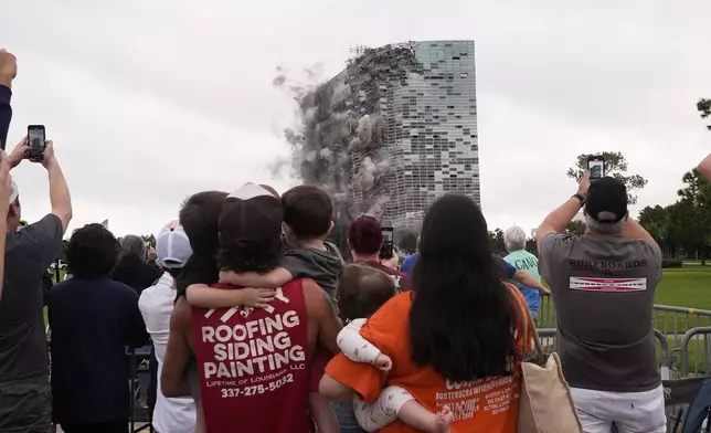 Tuff Gary, left, and Morgan LeBlanc with their children Hudson, Tuff, Jr., and Zander, of Jenning, La., watch the implosion of the Hertz Tower, that was heavily damaged after Hurricanes Laura and Delta in 2020, in Lake Charles, La., Saturday, Sept. 7, 2024. (AP Photo/Gerald Herbert)