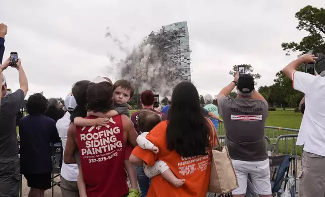 Tuff Gary, left, and Morgan LeBlanc with their children Hudson, Tuff, Jr., and Zander, of Jenning, La., watch the implosion of the Hertz Tower, that was heavily damaged after Hurricanes Laura and Delta in 2020 in Lake Charles, La., Saturday, Sept. 7, 2024. (AP Photo/Gerald Herbert)