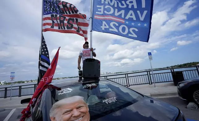 CORRECTS SPELLING OF JESTIN NEVAREZ - Jestin Nevarez, of Lake Worth, Fla., puts up flags on his vehicle outside the Mar-a-Lago estate after the apparent assassination attempt against Republican presidential nominee and former President Donald Trump in Palm Beach, Fla., Monday, Sept. 16, 2024. (AP Photo/Lynne Sladky)