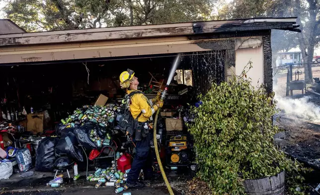 Firefighter Nolan Graham sprays water on a garage scorched by the Boyles fire in Clearlake, Calif., on Sunday, Sept. 8, 2024. (AP Photo/Noah Berger)