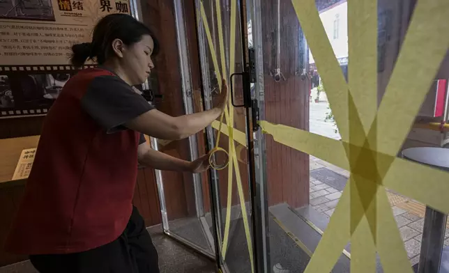 In this image released by Xinhua News Agency, a worker reinforces a glass window with tape at a cafe after the State Flood Control and Drought Relief Headquarters raised its emergency response for flood and typhoon prevention for Typhoon Yagi, Thursday, Sept. 5, 2024, in Haikou, south China's Hainan Province. (Pu Xiaoxu/Xinhua via AP)