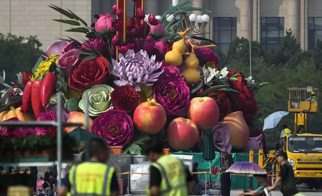 Visitors walk by workers installing a giant basket decorated with replicas of flowers and fruits on display at Tiananmen Square for the upcoming National Day celebration, in Beijing, Thursday, Sept. 19, 2024. (AP Photo/Andy Wong)