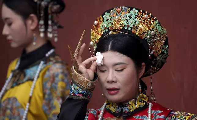 A Chinese woman dressed in Qing Dynasty attire wipes her sweat while posing for photographs near the Forbidden city in Beijing, China, Sunday, July 21, 2024. (AP Photo/Vincent Thian)